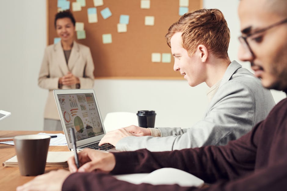 A diverse team of professionals in an engaging meeting, using laptops and notes for brainstorming.