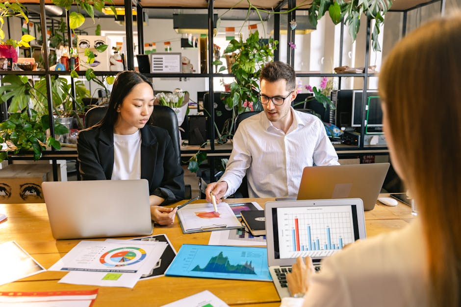 A diverse group of professionals collaborating in a business meeting with laptops and charts in a modern office setting.